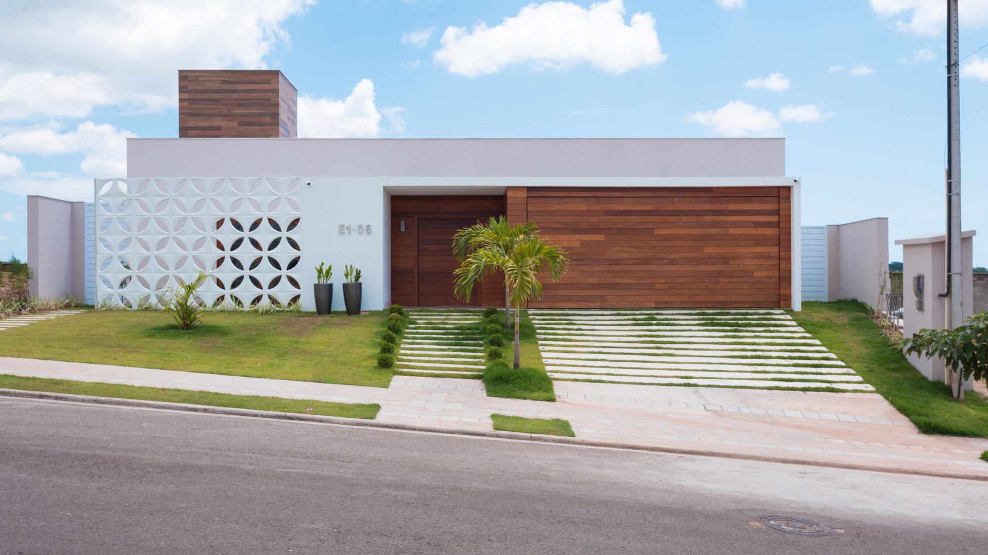 A fachada da casa possui linha retas, limpas e contemporâneas. A entrada é marcada pelo pórtico
branco e de madeira, que se contrapõe à leveza do cobogó cerâmico branco que resguarda o ambiente
do escritório do sol poente.