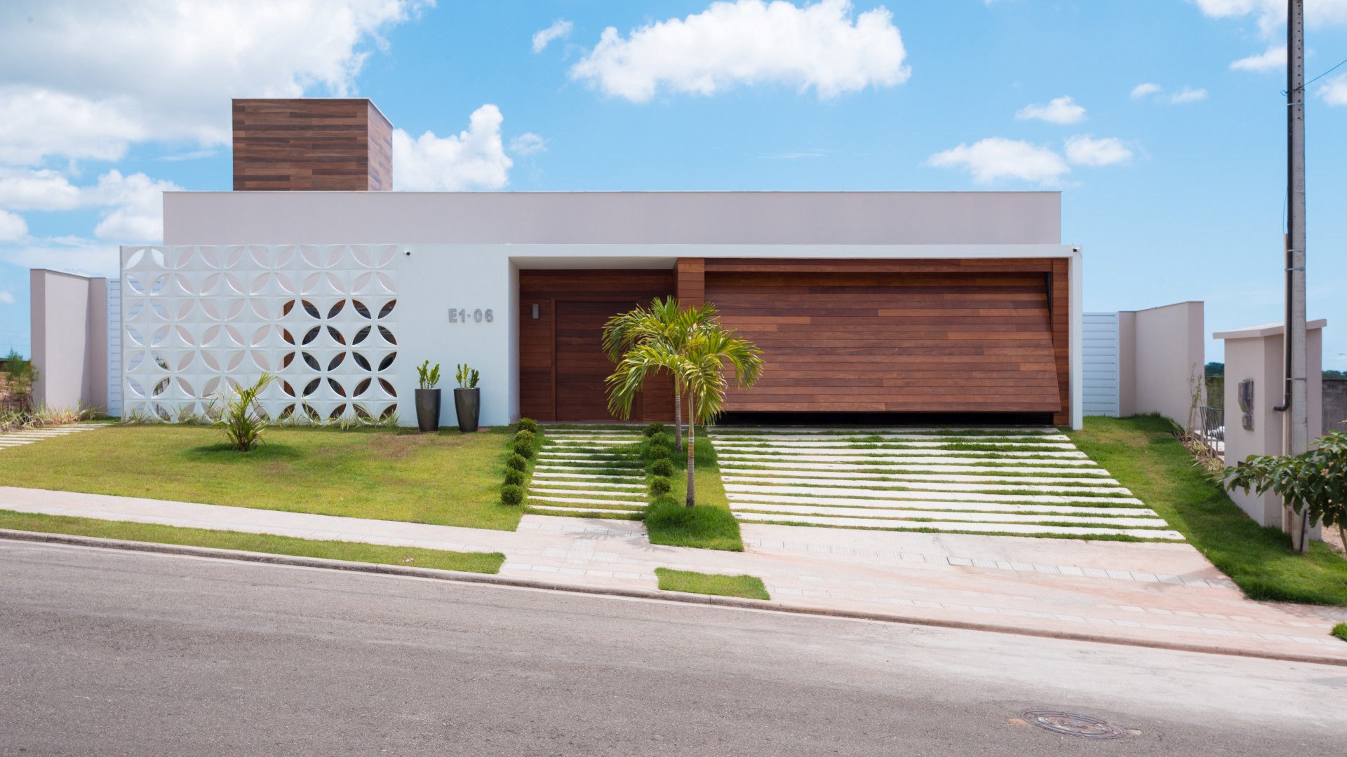A fachada da casa possui linha retas, limpas e contemporâneas. A entrada é marcada pelo pórtico
branco e de madeira, que se contrapõe à leveza do cobogó cerâmico branco que resguarda o ambiente
do escritório do sol poente.