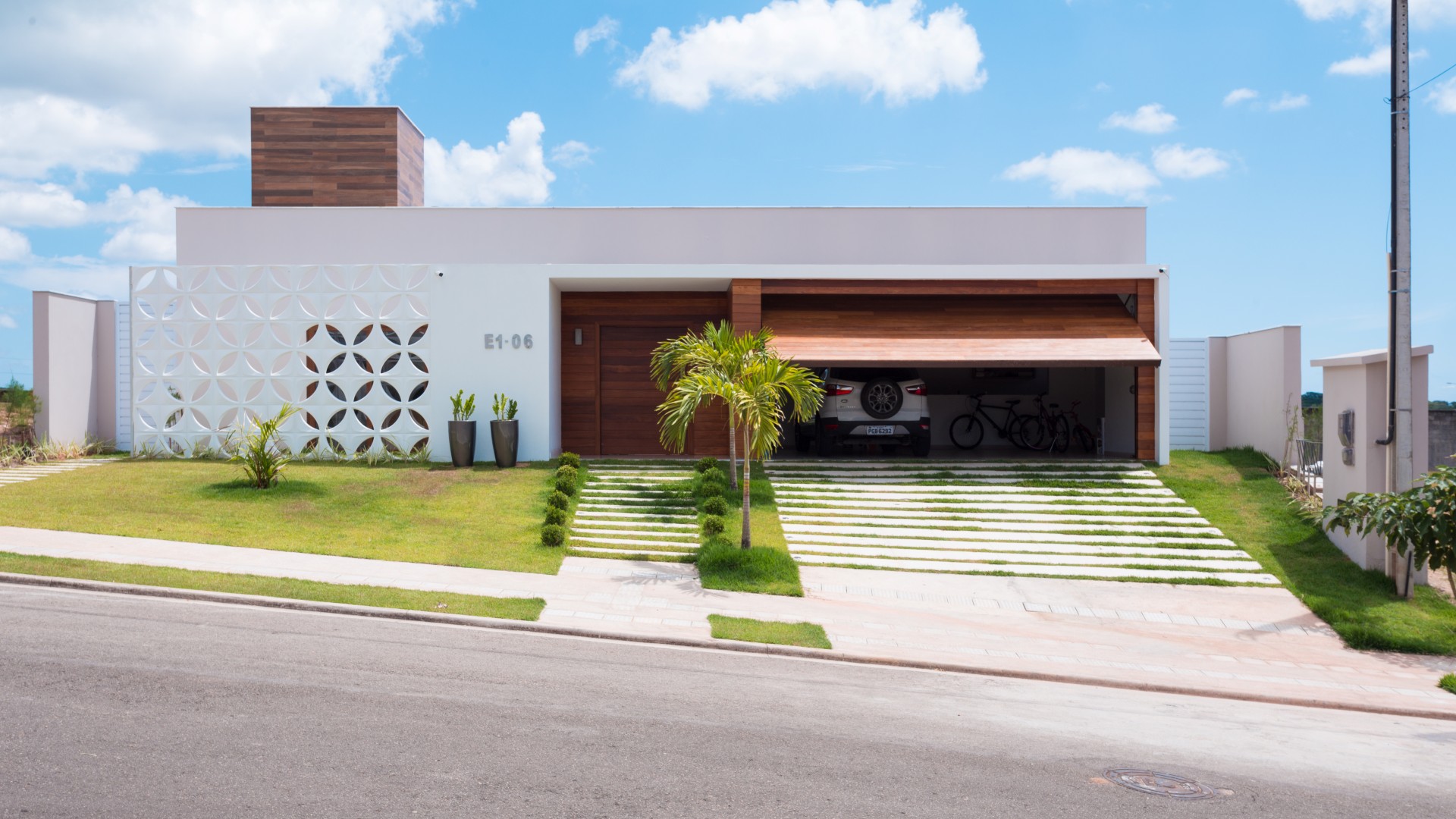 A fachada da casa possui linha retas, limpas e contemporâneas. A entrada é marcada pelo pórtico
branco e de madeira, que se contrapõe à leveza do cobogó cerâmico branco que resguarda o ambiente
do escritório do sol poente.