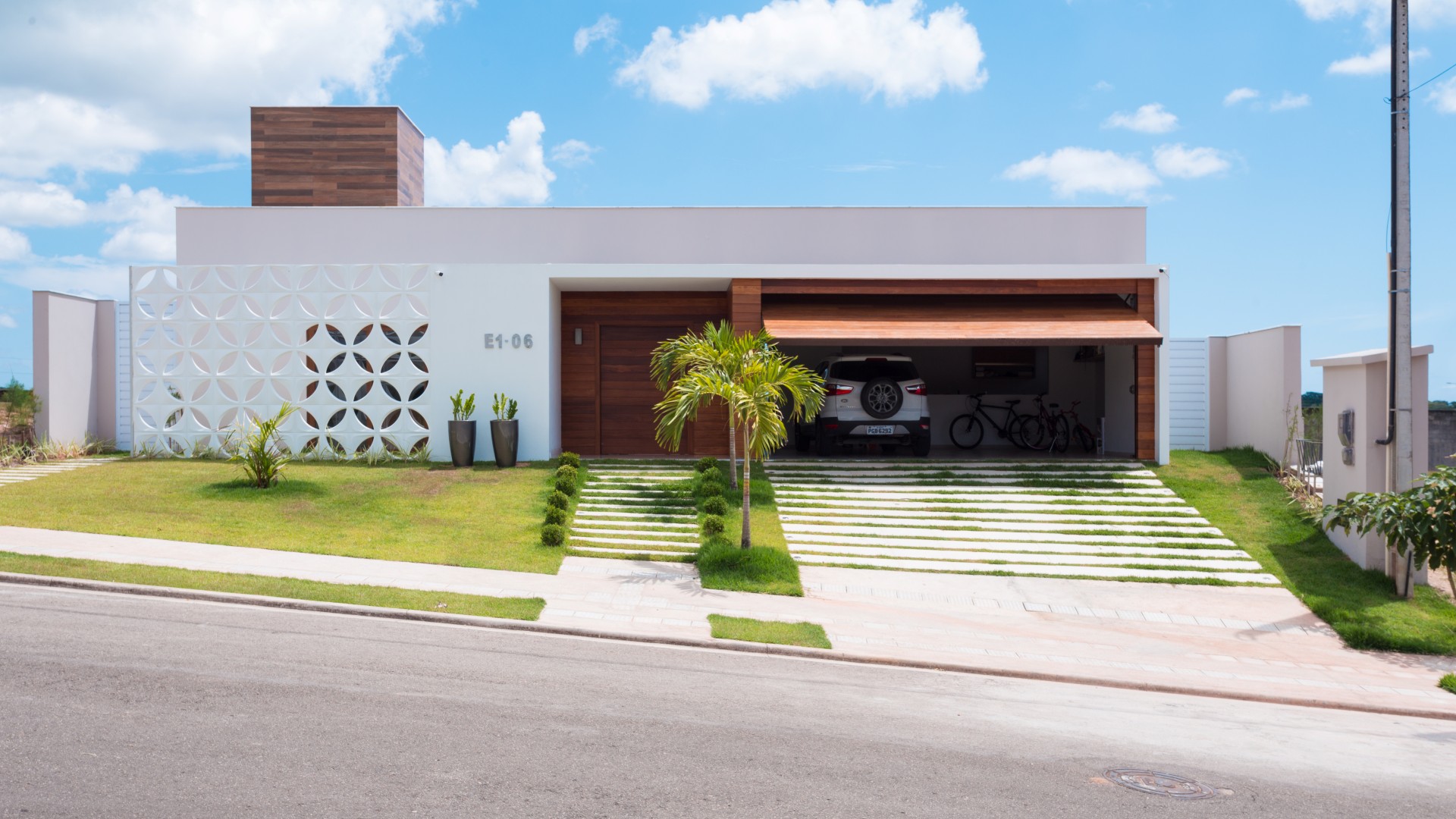 A fachada da casa possui linha retas, limpas e contemporâneas. A entrada é marcada pelo pórtico
branco e de madeira, que se contrapõe à leveza do cobogó cerâmico branco que resguarda o ambiente
do escritório do sol poente.
