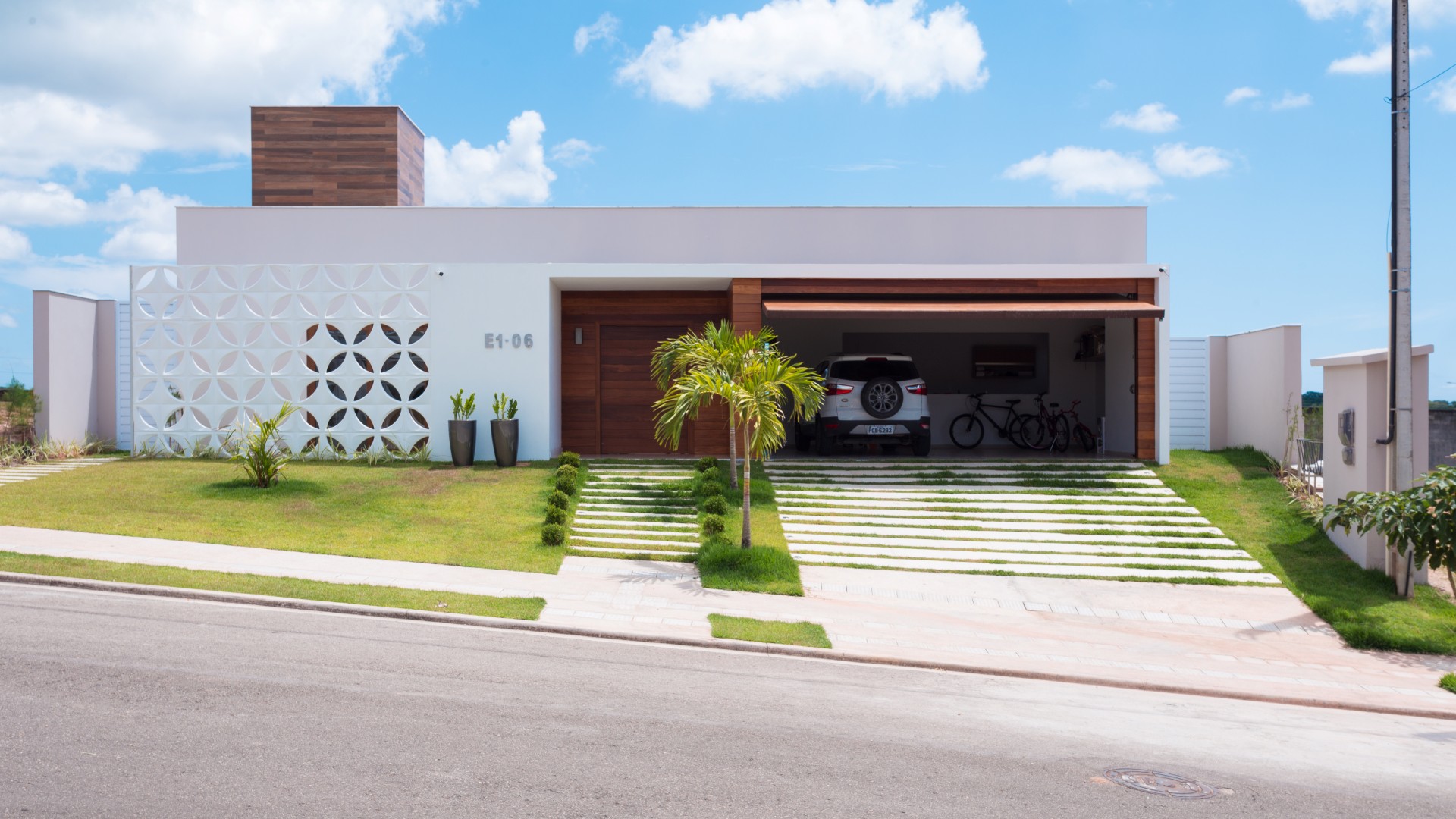 A fachada da casa possui linha retas, limpas e contemporâneas. A entrada é marcada pelo pórtico
branco e de madeira, que se contrapõe à leveza do cobogó cerâmico branco que resguarda o ambiente
do escritório do sol poente.